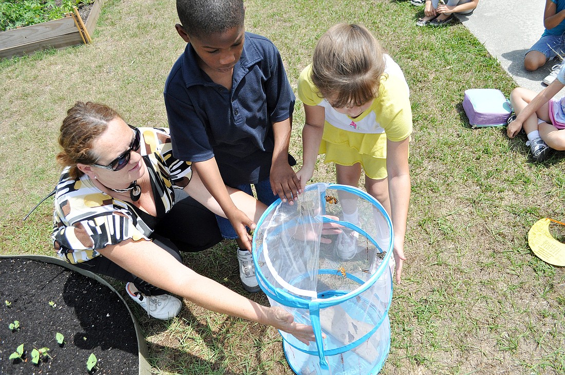 Teacher Annette Thompson helps students Javon Holmes and Heather Parker release butterflies in the garden at Bunnell Elementary School. PHOTO BY SHANNA FORTIER