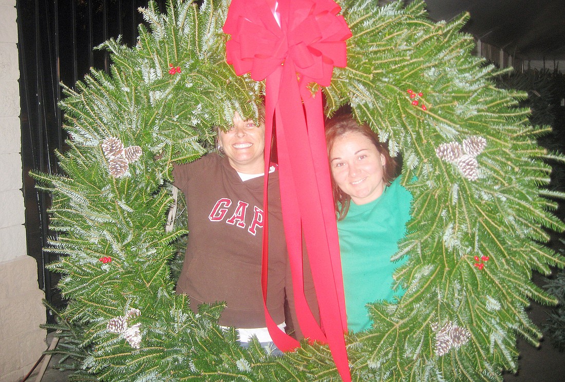 Julie Raulerson and Melissa Ziem stand inside a massive holiday wreath.