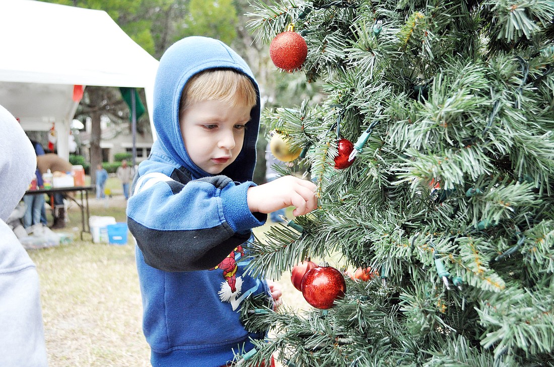 Nathaniel Harvey places an ornament on the Christmas tree in the Holidays Around the World play area.