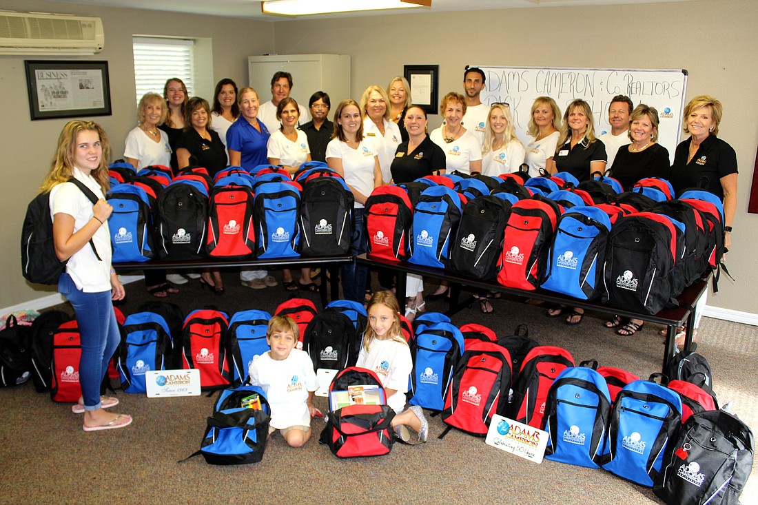 Adams Cameron Realtors in Ormond Beach, pose with some of their children, and backpacks filled with school supplies for less fortunate students. Photo by Jacque Estes