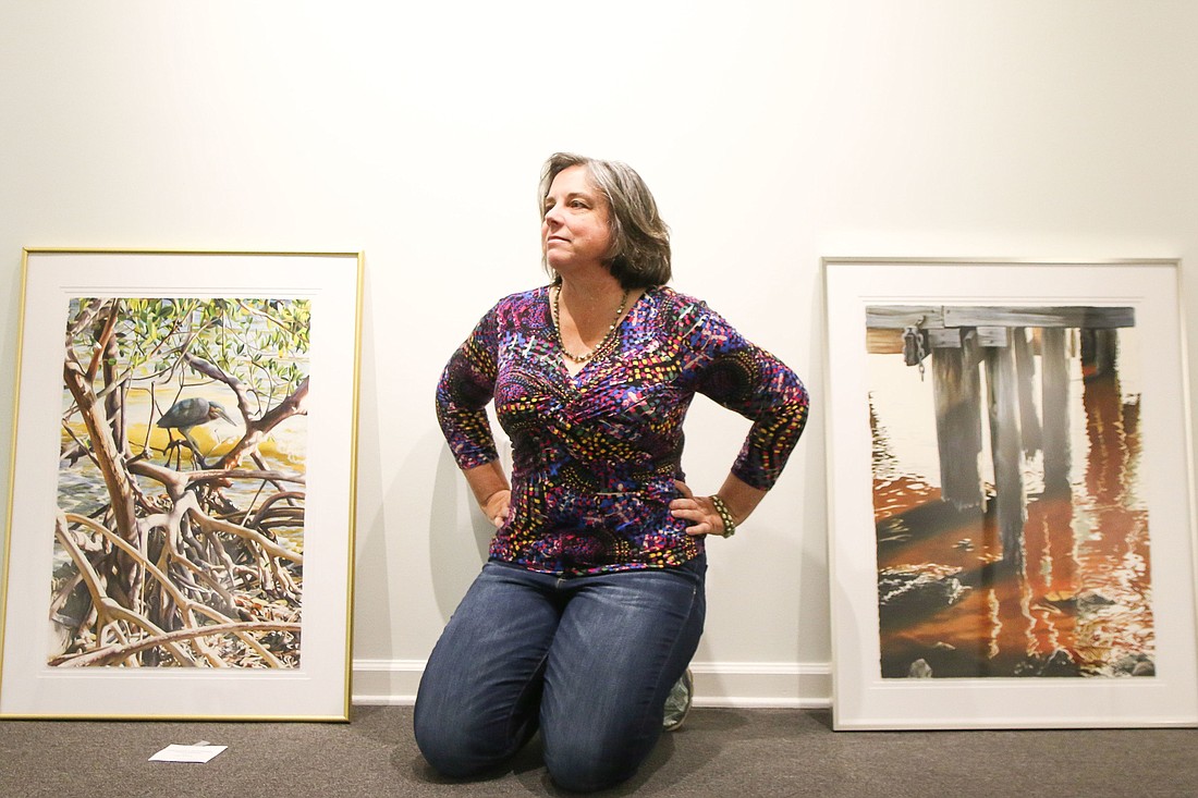 Leigh Murphy sits between her paintings "Mangrove Mysteries, Green Heron" and "Ortega River Dock" in the Ormond Memorial Art Museum before the exhibit gets hung. Photo by Paige Wilson