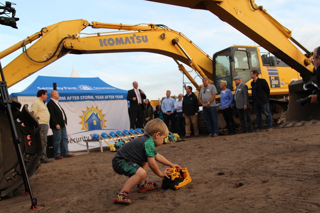 Hunter Bradley, 3, plays with his yellow toy bulldozer as Ormond Beach Mayor Bill Partington speaks during Security First's groundbreaking ceremony for its new headquarters on March 7. Photo by Jarleene Almenas