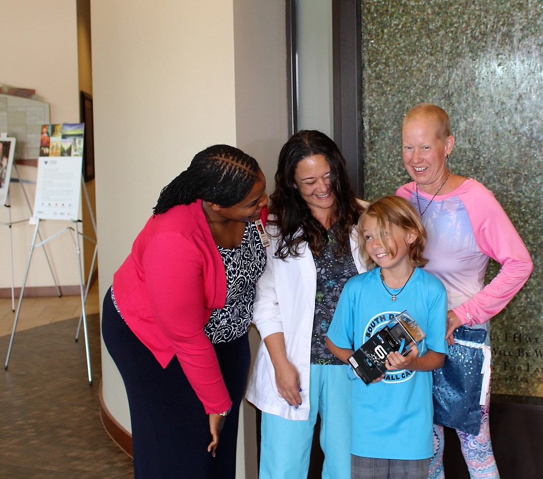Eli Burgess opens a gift at Florida Hospital Memorial Medical Center. His mother, Lisa Burgess (right), is fighting cancer. Also shown are hospital chaplain Loreal McInnes and nurse practitioner Amy Youman. Courtesy photo