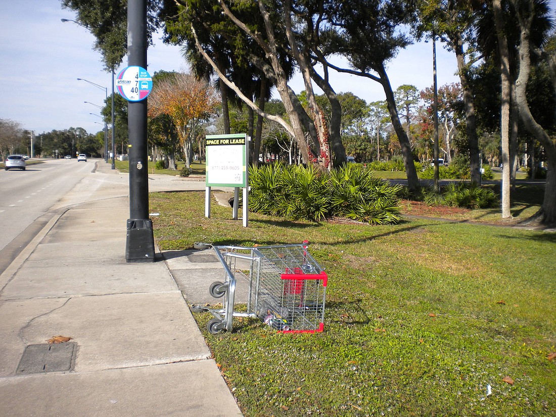 A flipped shopping cart with trash inside sits by a bus stop on Nova Road in Port Orange. Photo by Tanya Russo.