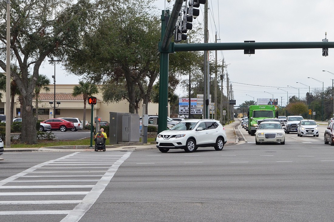 A man in a wheelchair crosses the street while a car waits to turn. .