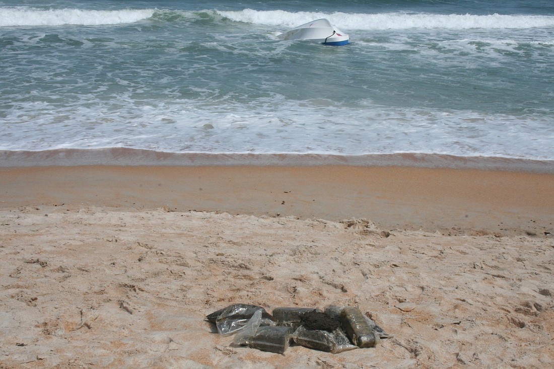 Several bricks of marijuana sit on the beach near the capsized boat, under watch of officials from the Florida Fish and Wildlife Conservation Commission and the Flagler County Sheriff's Office.