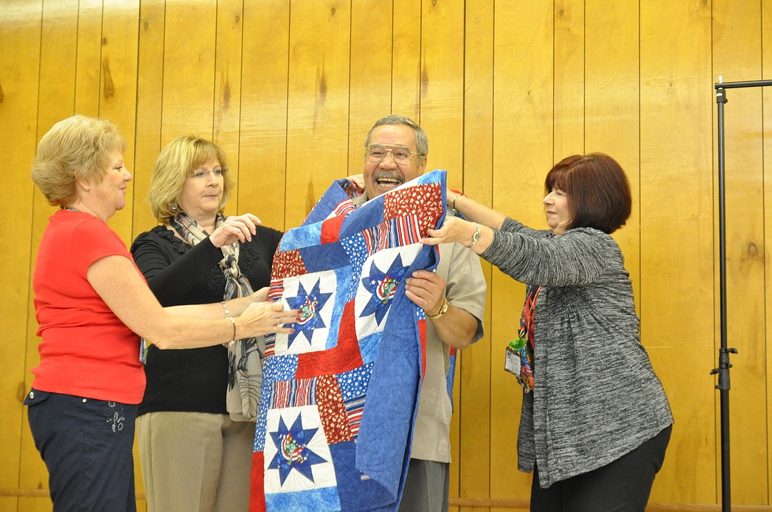 Peggy Manley, Cheryl Roark and Marie Garelli wrap Vietnam War Veteran Nelson Acevedo in his newly donated blanket.