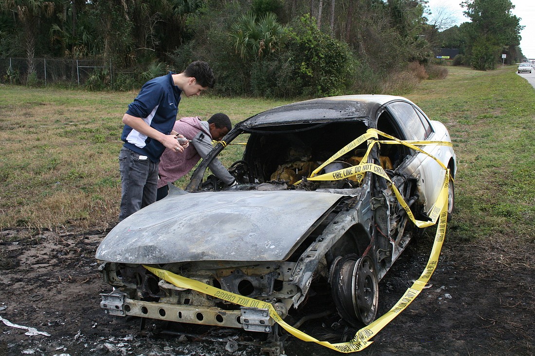 Nikko Bembry and Manniee Torres rifle through the burnt frame of Bembry's car, salvaging as many items as they can.