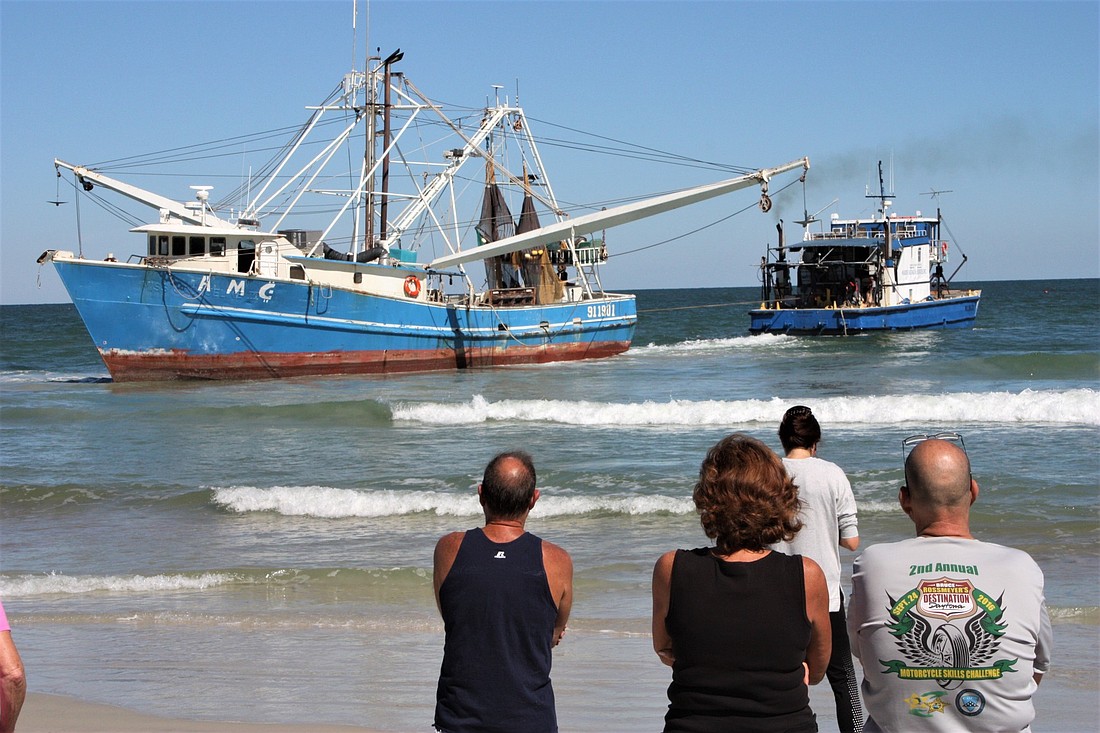 A crowd watches a tow boat attempt to remove the shrimp boat from the beach. File photo