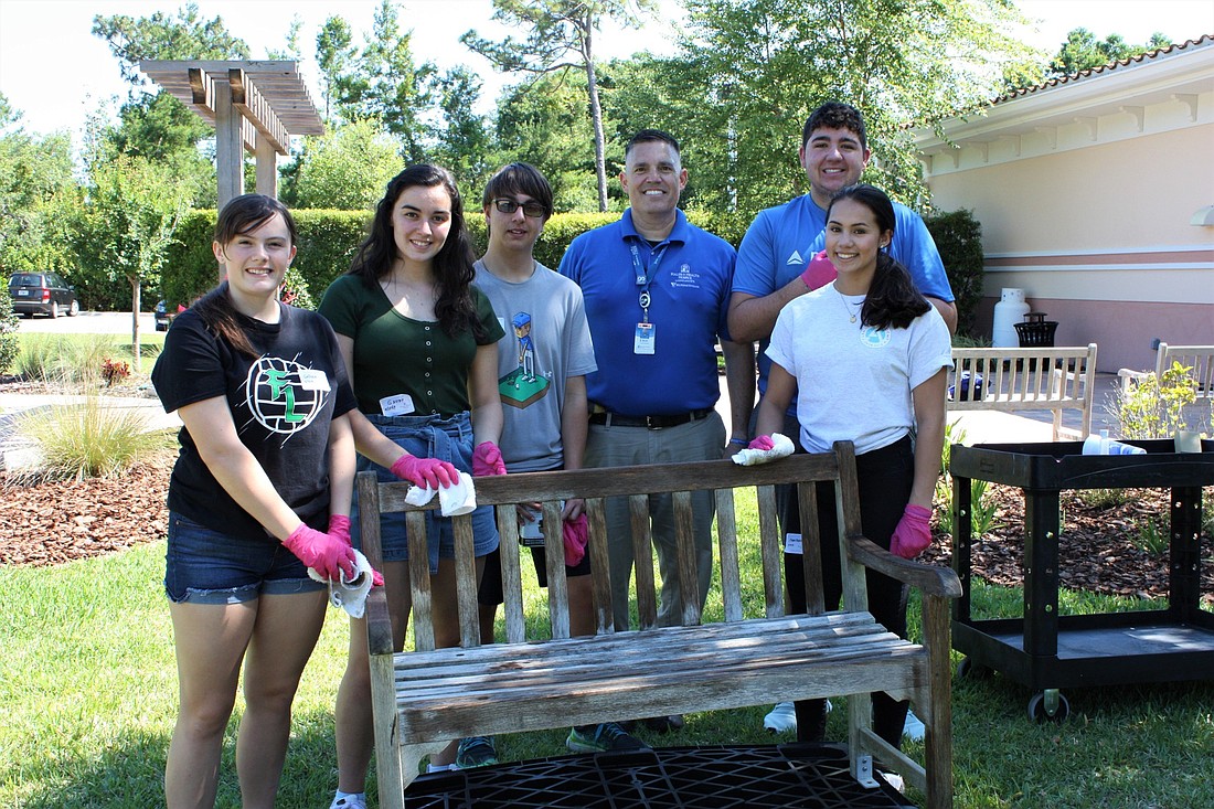 Father Lopez High School students stain a bench they are donating to Halifax Heath Hospice. Shown are Colleen Coughlin, Gabriella Peburn, Antonio Moreno, Hospice Operations Manager Eric Whitwam, Dante Picchiello and Flynn Baliton. Photo by Wayne Grant
