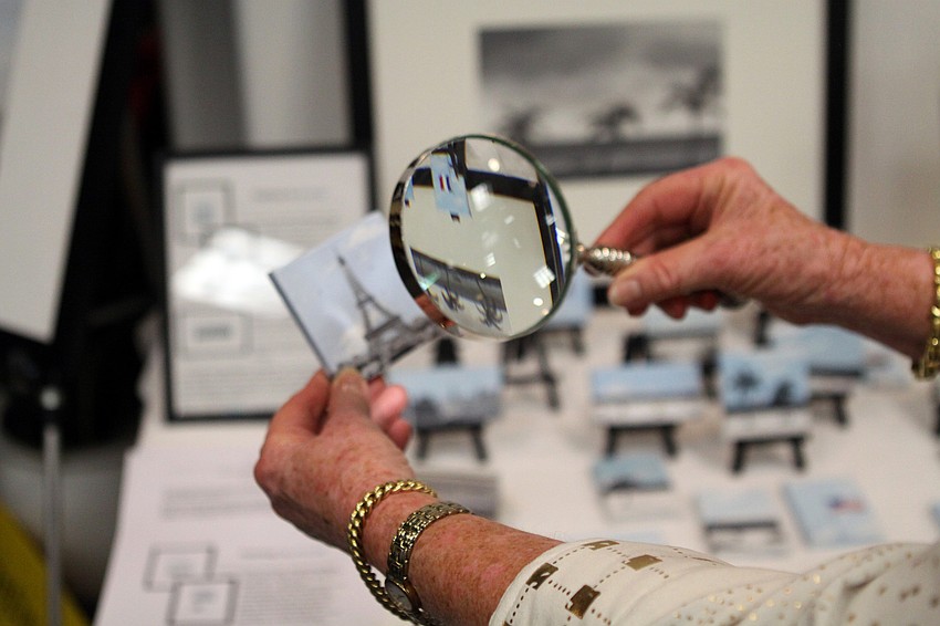 Fiona Lohrisch looks through a magnifying glass to see the great detail put into the miniature paintings created by Francoise “frenchie” Mandonnaud Stotts.