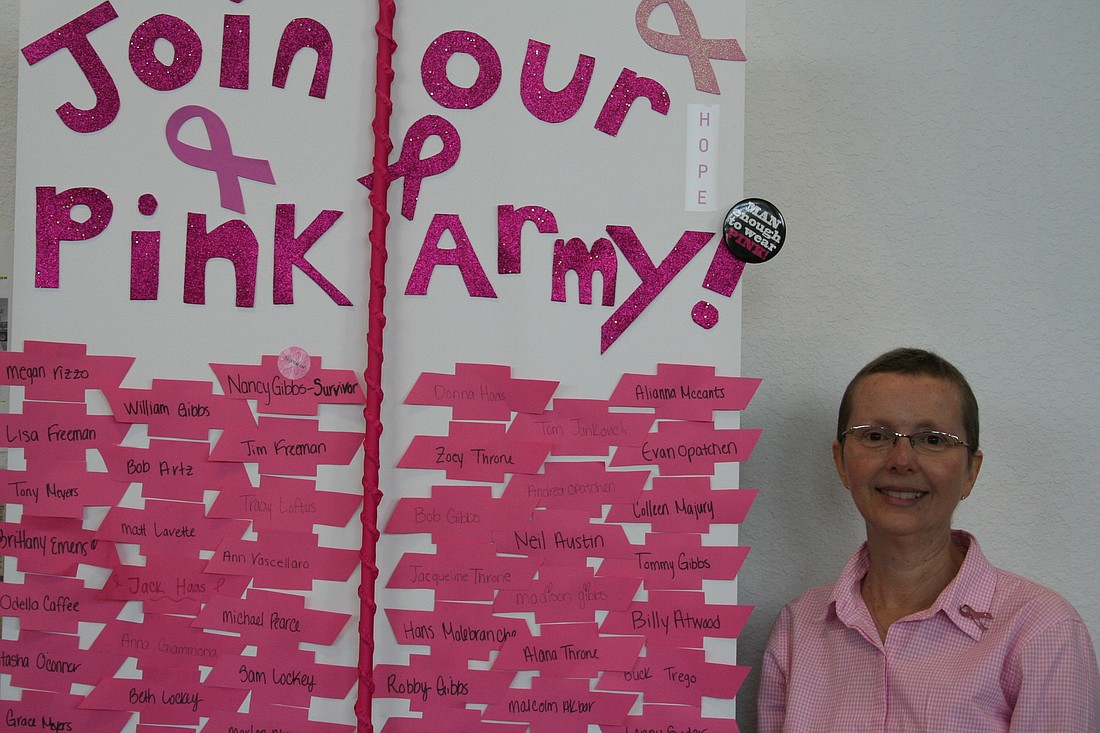 Nancy Gibbs stands in front of a sign at Tom Gibbs Chevrolet naming the dealership's Pink Army team members.
