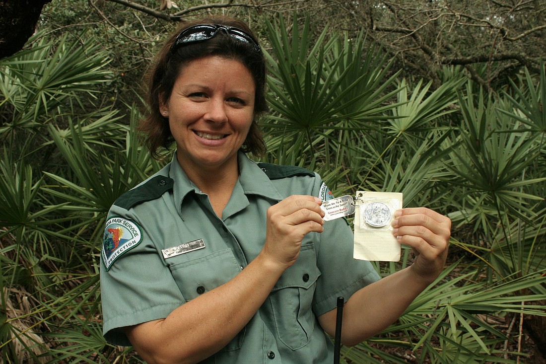 Park Ranger Jennifer Giblin holds up a Masonic coin hidden in a geocache at Gamble Rogers Memorial State Recreation Area. (Photo by Jonathan Simmons)