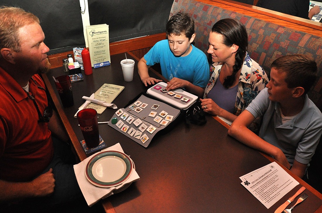 Zach Robich, a non-verbal autistic student at Belle Terre Elementary School, uses his ProxTalker communication device to tell his parents Delisa and Rich what he would like to eat. His older brother, Rex, records all of his brother's sound tags for him.