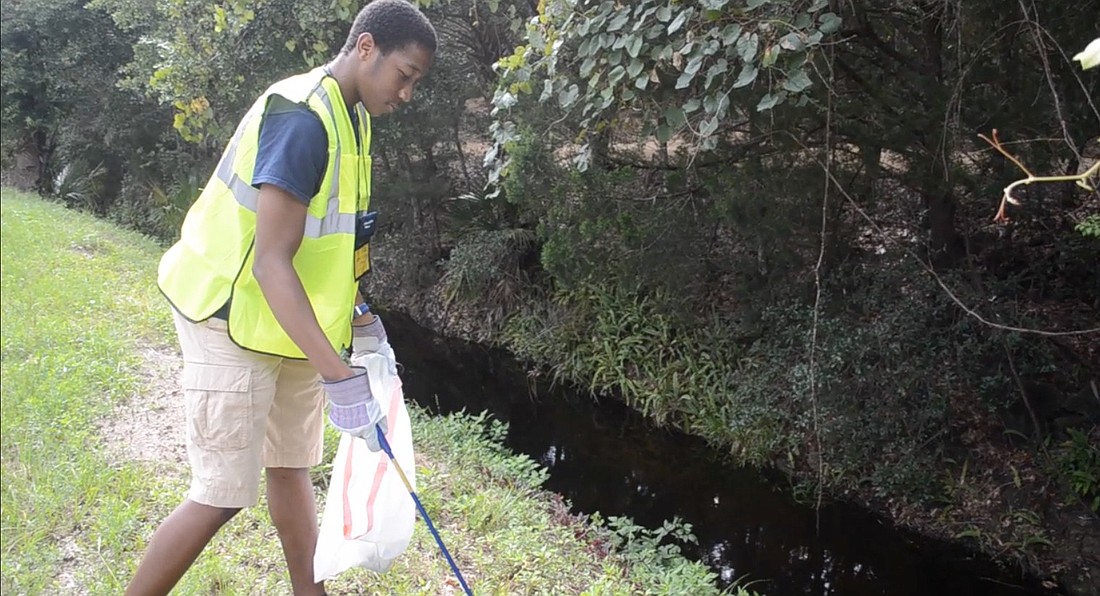Davon Taylor picks up trash from the side of Mala Compra Road in the Hammock area.