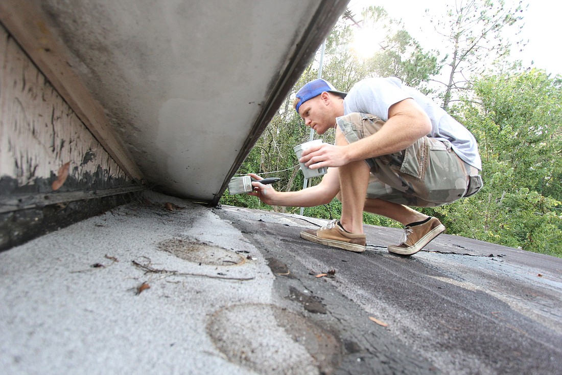 Jordan Farrell paints the roof of one of the four homes on Hymon Circle in Bunnell getting a fresh coat of paint. PHOTOS BY SHANNA FORTIER