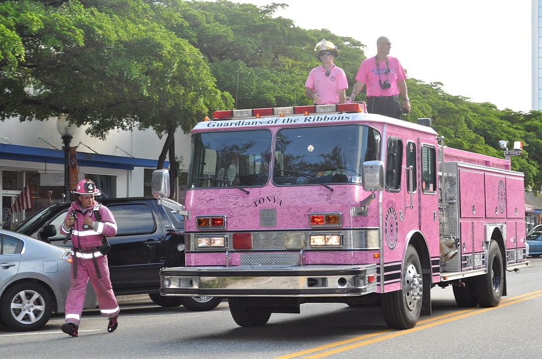 A local firefighter jogs beside one of four pink firetrucks.