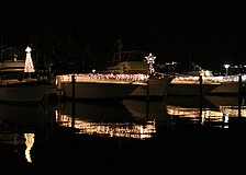 Three boats decorated in white lights reflect back in the water during Bird Key Yacht Clubâ€™s Lighting of the Fleet evening.