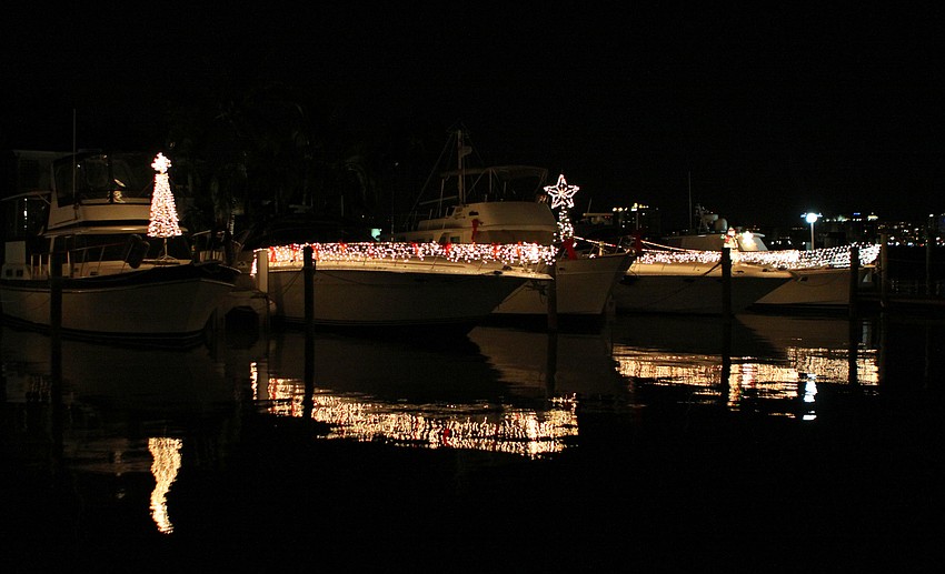 Three boats decorated in white lights reflect back in the water during Bird Key Yacht Clubâ€™s Lighting of the Fleet evening.