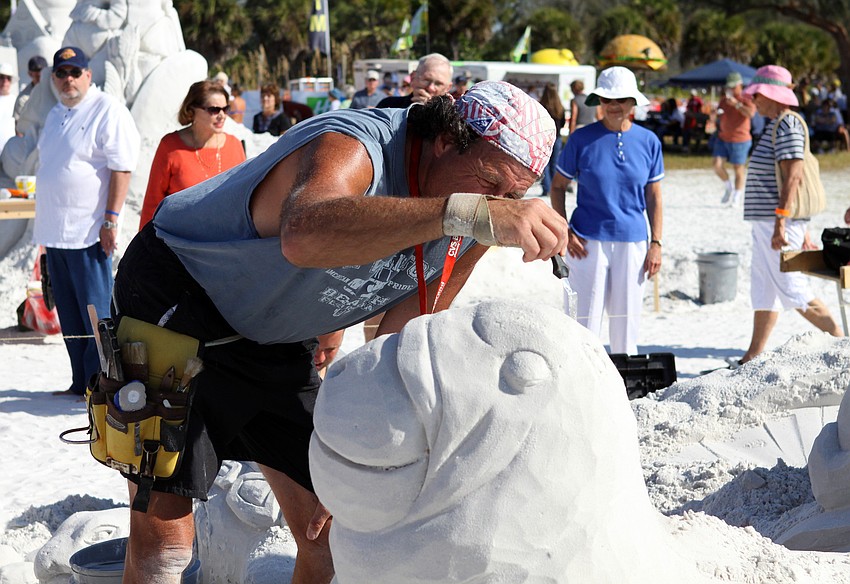 Steve Topazio does some careful detail work on his sand sculpture as beachgoers look on.