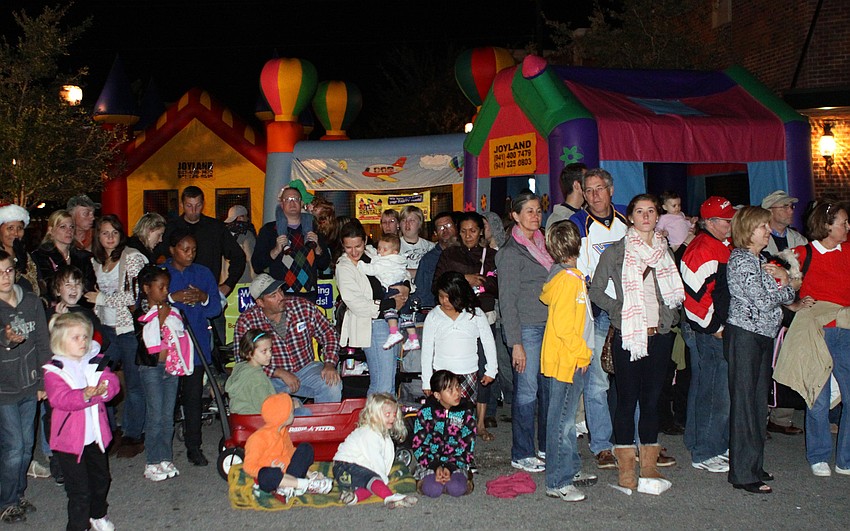 The crowd watches the parade go by while some kids play in the three bounce houses behind the crowd.