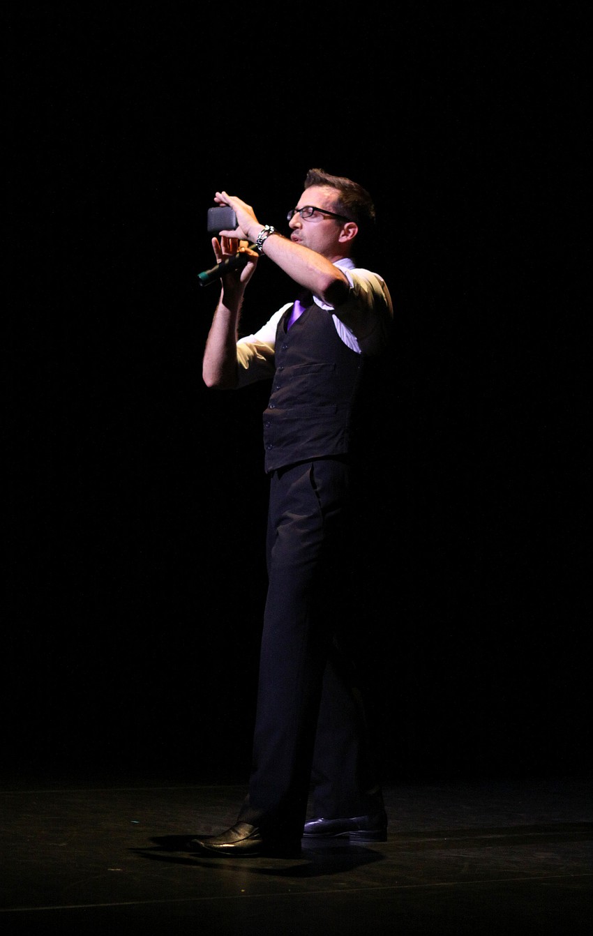 Joey Panek, Master of Ceremonies, takes a photo on his phone of the audience to post to his various social media sites.