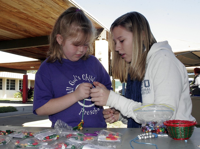 Braden River High junior Peyton Weigel helps 6-year-old Hannah Rudolph make a holiday necklace.