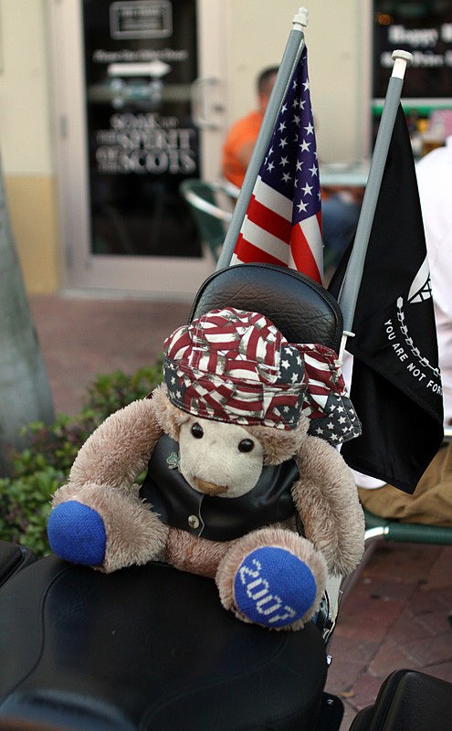 A stuffed teddy bear sits on the back of a motorcycle.