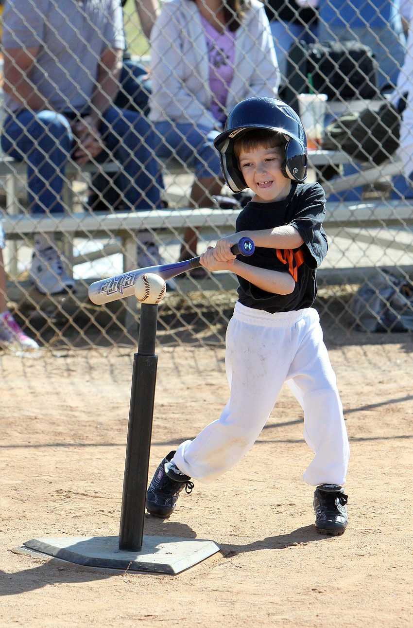 A smiley T-ball player for the Giants whacks the ball off the tee.