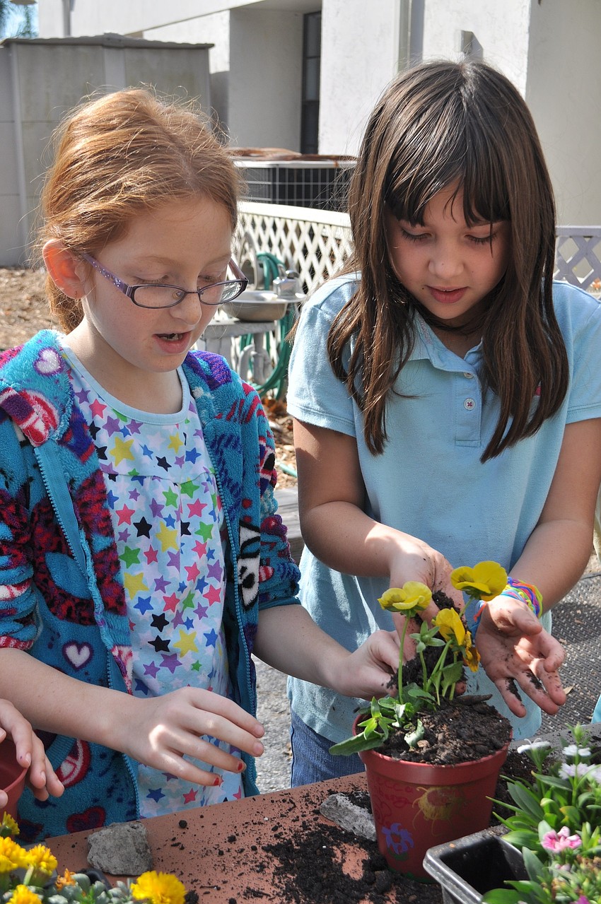 Julia Steinbach, right, helps Rebecca Kleinberg plant a flower.