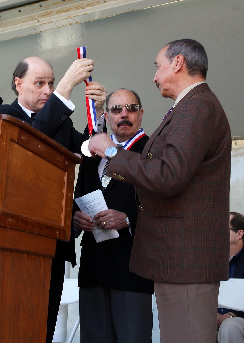 Chuck Sidlow holds out Alberto Ataydeâ€™s medal as Andres Atadye looks on, during the induction ceremony on Sunday.