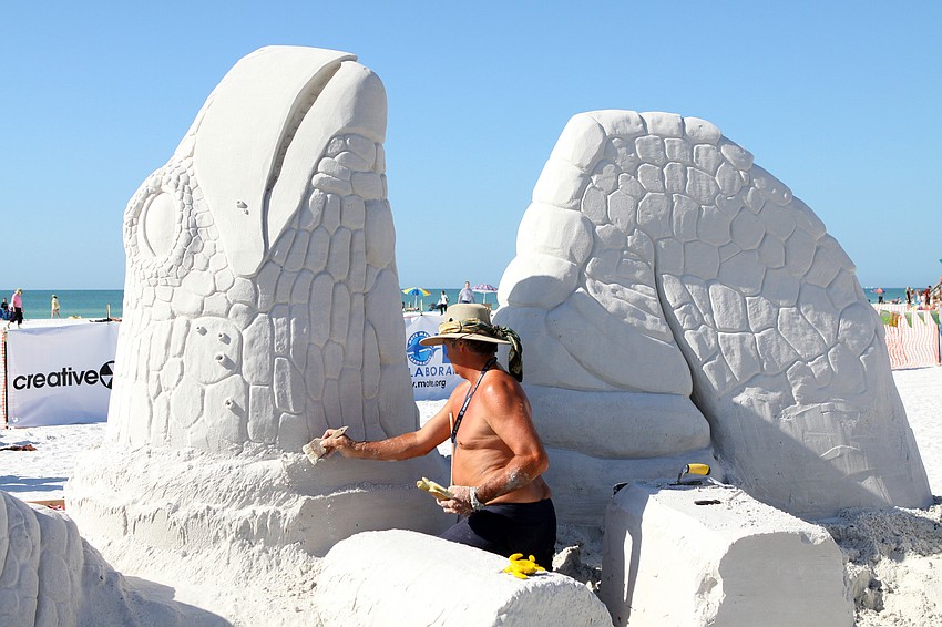 John Gowdy works on brushing away some extra sand around the head of the sea turtle that was part of his sand sculpture with Matt Deibert.