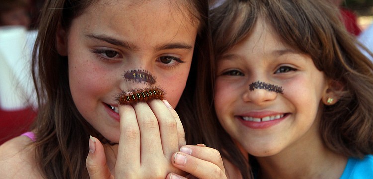 Trinity Redhead and Arianne Shedlock, 8, hold up the caterpillar they found during the Earth Day Celebration. The girls also had caterpillars painted across their noses and named their new friend "Tatty".