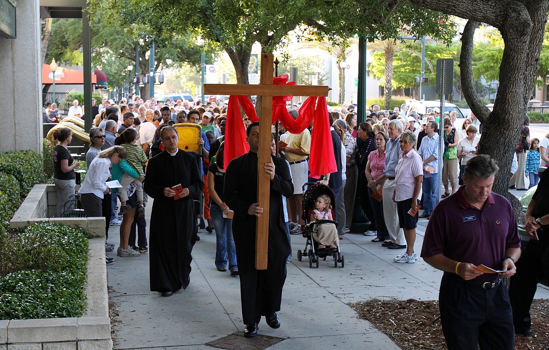People follow the cross down Main Street while singing "Holy God" as they make their way from station to station Friday, April 22,  during the Stations of the Cross event.