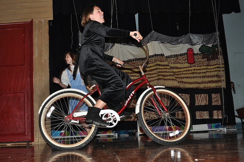 Caught up in the tornado, Brianna McVaugh, acting as Miss Almira Gulch, rides her bicycle across the stage.