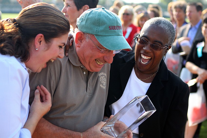 County Commissioners Christine Robinson and Carolyn Mason smile and laugh as they surrounded a teary Norman Schimmel after he was surprised during the 2011 National Tourism Week Awards ceremony and given the â€œVoice of Tourismâ€ Award.