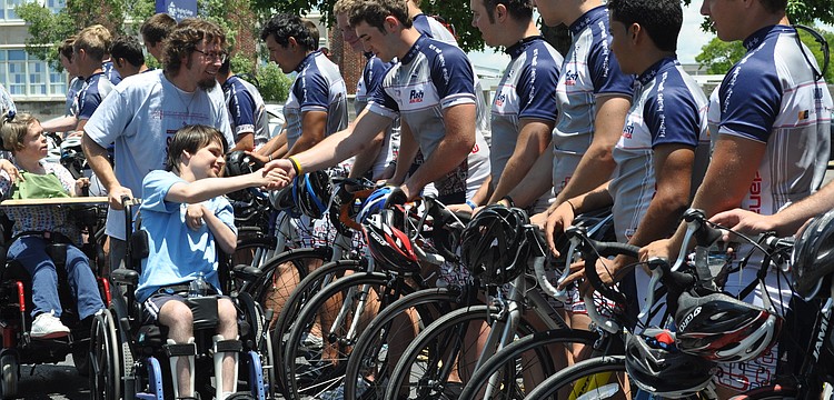 Alex Palmer, pushed by Jason Rawley of UCP, shakes hands with Chris Papa of Pi Kappa Phi and Gear Up America.