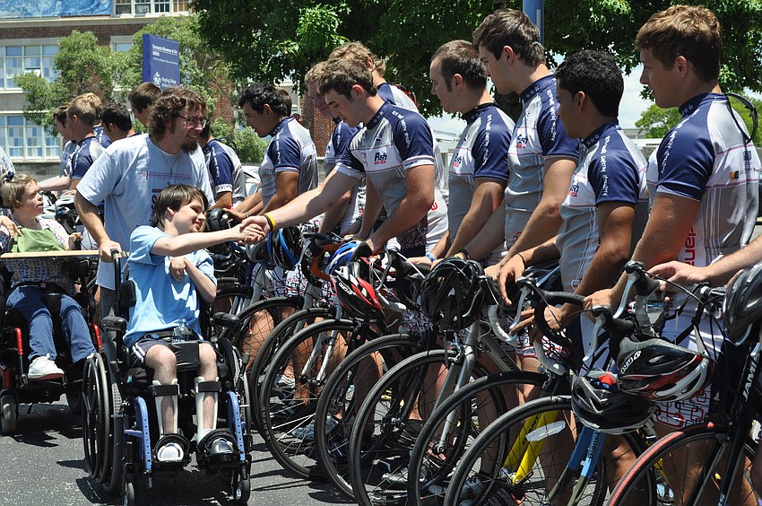 Alex Palmer, pushed by Jason Rawley of UCP, shakes hands with Chris Papa of Pi Kappa Phi and Gear Up America.