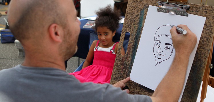 Lauren Frisbie, 6, sits while Rafael Diez does a free caricature of her at the Kaufman, Englett & Lynd booth at the Craft Festival Sunday, May 22 along Main Street and in Five Points Park.