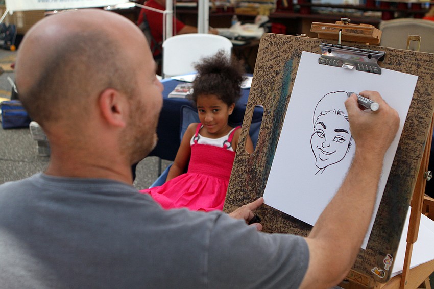 Lauren Frisbie, 6, sits while Rafael Diez does a free caricature of her at the Kaufman, Englett & Lynd booth at the Craft Festival Sunday, May 22 along Main Street and in Five Points Park.