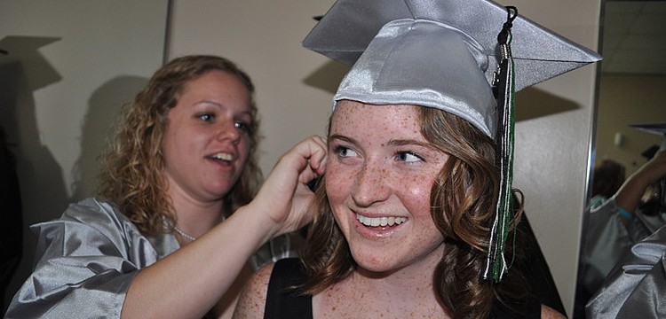 Breanna Howell, behind, helps Emily Wray pin on her cap.