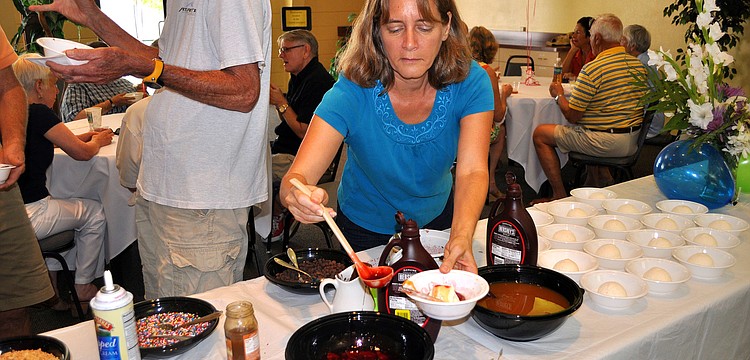 Joann McManus puts some strawberries on top of her ice cream Sunday, August 14 during the ice cream social in the Parish Hall at St. Boniface.