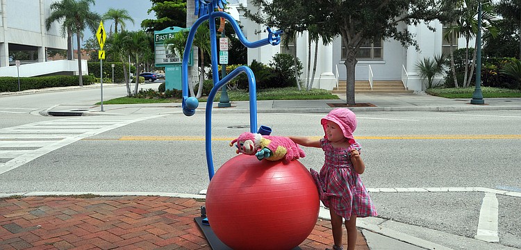 Benita Mayer, 2 1/2, lets her caterpillar toy, Lena, crawl on the balance ball under the Tube Dude's foot outside of Gymmery's Fitness Wear on Main Street. Mayer and her family are visiting from Frankfurt, Germany.