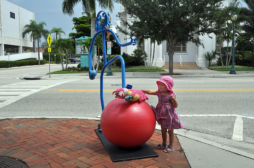 Benita Mayer, 2 1/2, lets her caterpillar toy, Lena, crawl on the balance ball under the Tube Dude's foot outside of Gymmery's Fitness Wear on Main Street. Mayer and her family are visiting from Frankfurt, Germany.