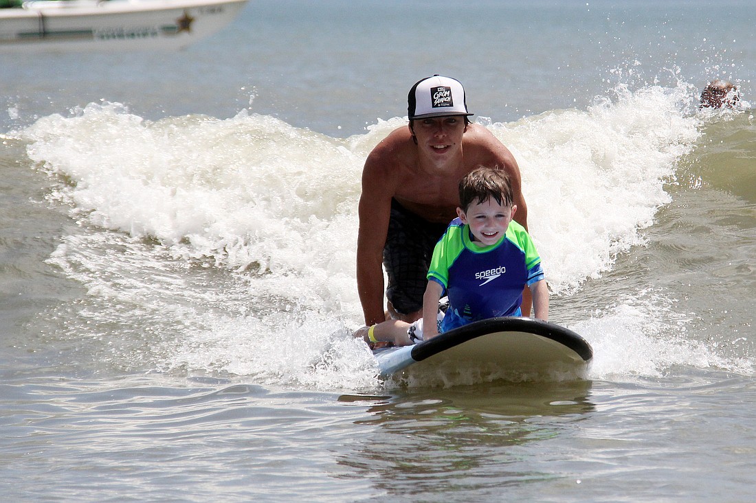 Caleb Crockett catches a wave with the help of volunteer Logan Hayes at the Surfers for Autism event held in Flagler Beach Saturday. PHOTOS BY SHANNA FORTIER