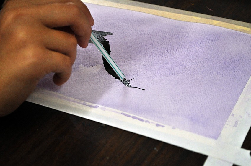 A student blows on the wet paint to create tree branches and limbs.