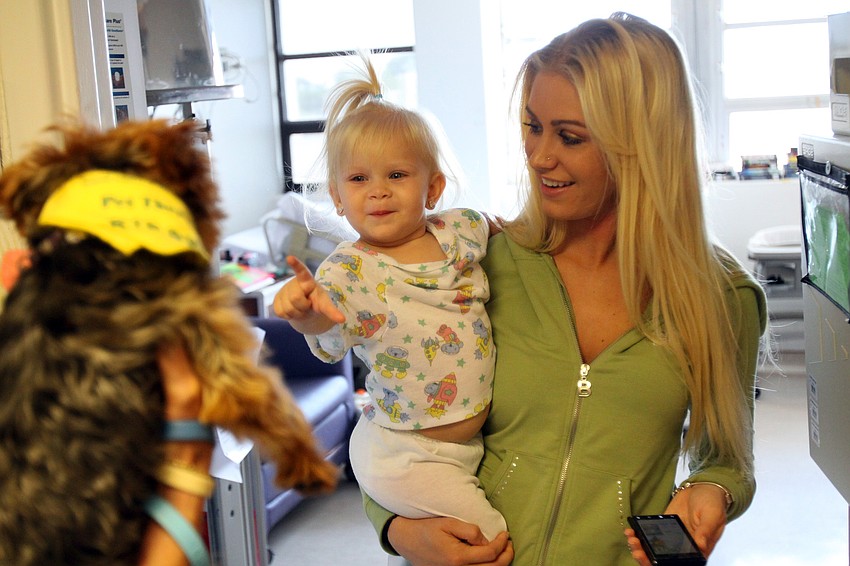 Heidee Regan points at Kirby and smiles while her mom, Nicole, holds her up to see the dog Thursday, May 12 at Sarasota Memorial Hospital. Regan was unable to touch the dogs due to her condition and cried when the dogs left her doorway.