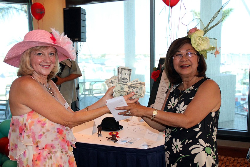 Mari Zevin hands Monica Jorque her winnings, $26.00, on Saturday, May 7 at the Kentucky Derby party at the Sarasota Yacht Club.