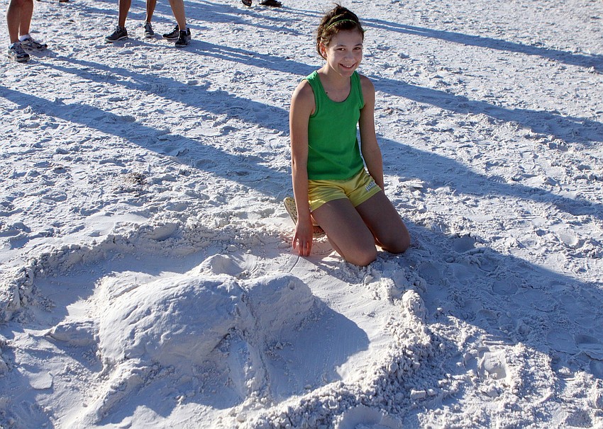 Nichole Pflanzer, 12, poses next to the turtle sand sculpture she made on Saturday, April 2 during the 25th Annual Run for the Turtles on Siesta Key Beach.