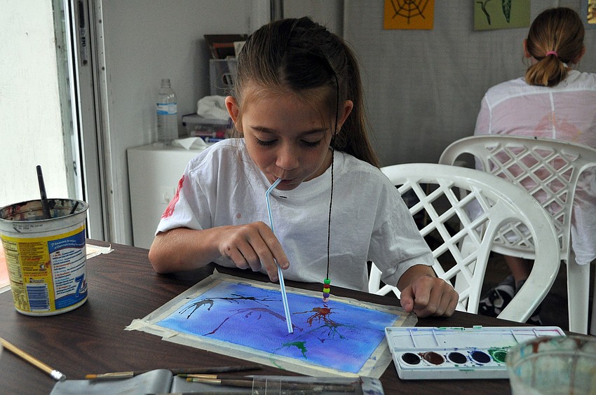 Sarah Andrews, 7, blows through a straw to make firework looking splotches on her canvas.